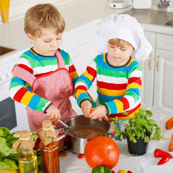 Pequeños gemelos cocinando sopa italiana y comida con verduras frescas —  Fotos de Stock