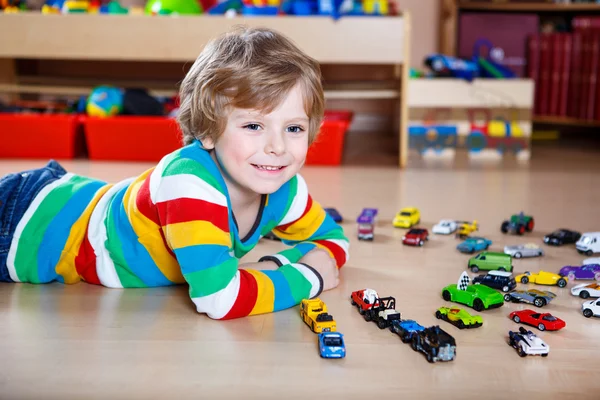 Забавный маленький мальчик играет с кучей игрушечных машин в помещении — стоковое фото