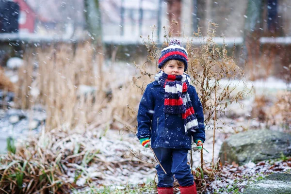 Cute little funny boy in colorful winter clothes having fun with — Stock Photo, Image