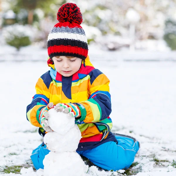 Precioso niño en ropa colorida haciendo un muñeco de nieve — Foto de Stock