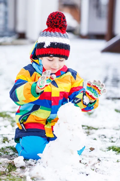 Funny preschool boy in colorful clothes making a snowman — Stock Photo, Image