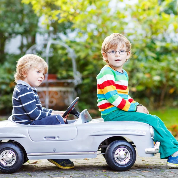 Два счастливых близнеца играют с большой старой игрушечной машиной в летнем саду, o — стоковое фото