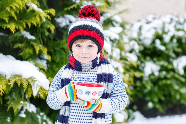 雪の結晶とホットチョコと大きなカップを保持している面白い小さな子供 — ストック写真