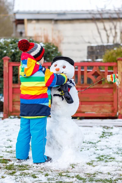 Funny kid boy i färgglada kläder att göra en snögubbe — Stockfoto