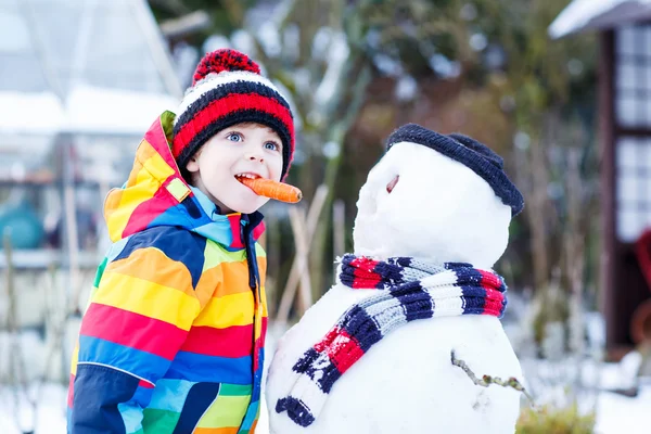 Enfant drôle garçon en vêtements colorés faire un bonhomme de neige, en plein air — Photo