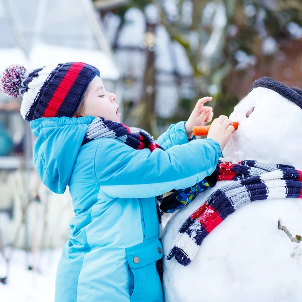 Lustige Junge in bunten Kleidern, die einen Schneemann, im Freien — Stockfoto