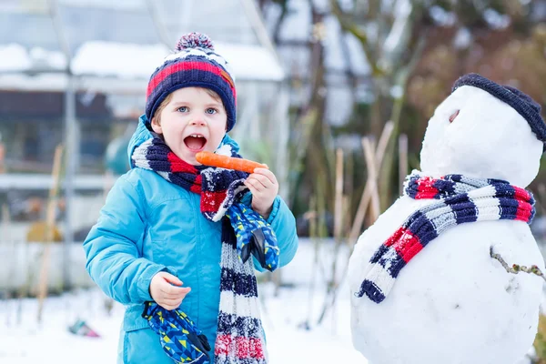 Funny kid boy i färgglada kläder att göra en snögubbe, utomhus — Stockfoto