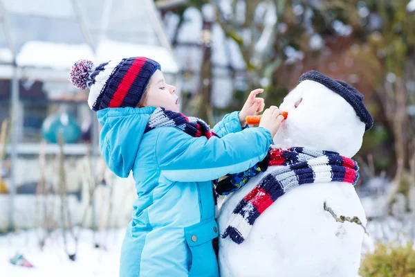 Niño gracioso en ropa colorida haciendo un muñeco de nieve, al aire libre — Foto de Stock