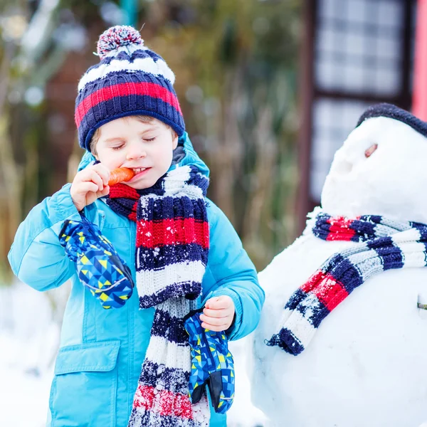 Niño gracioso en ropa colorida haciendo un muñeco de nieve, al aire libre — Foto de Stock