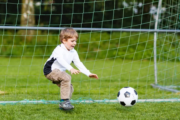 Two little sibling boys playing soccer and football on field