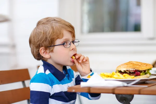 Kleine jongen eten fastfood: Franse frietjes en hamburger — Stockfoto