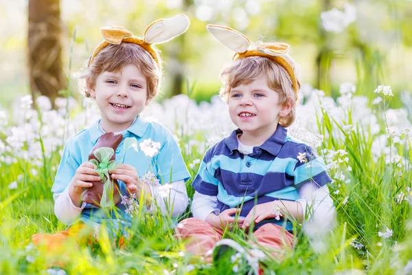 Dos niños pequeños usando orejas de conejo de Pascua y comiendo chocolate —  Fotos de Stock