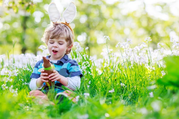 イースターのバニーの耳を身に着けていると、チョコを食べるかわいい幸せの小さな男の子 — ストック写真