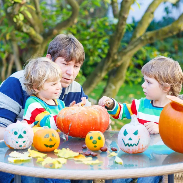 Papá joven y dos hijos pequeños haciendo Jack-o-linterna para hallowee — Foto de Stock