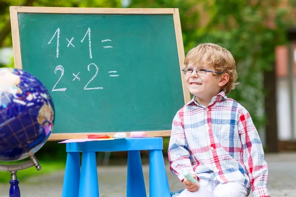 可爱的小小孩男孩戴着眼镜在黑板练习立体几何 — 图库照片