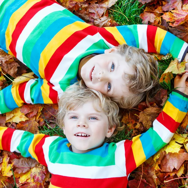 Two little kid boys laying in autumn leaves in colorful clothing — Stock Photo, Image