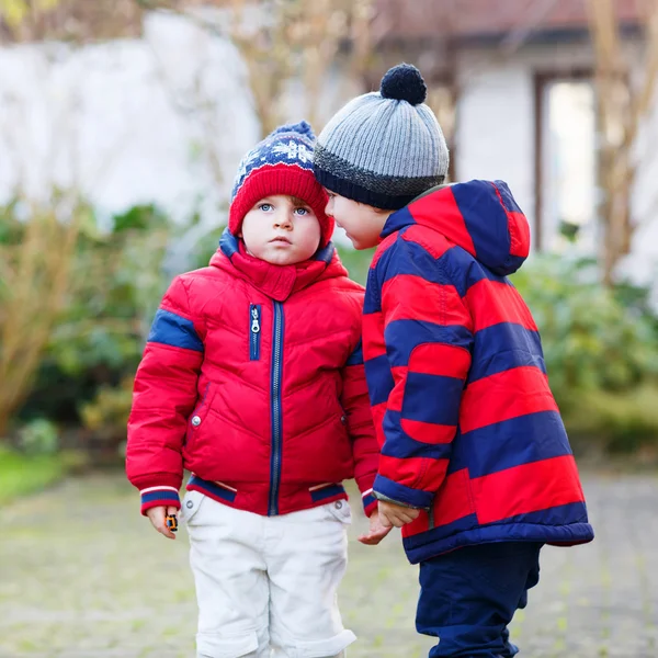 Dois meninos pequenos irmãos em jaquetas vermelhas e chapéus de inverno falando t — Fotografia de Stock