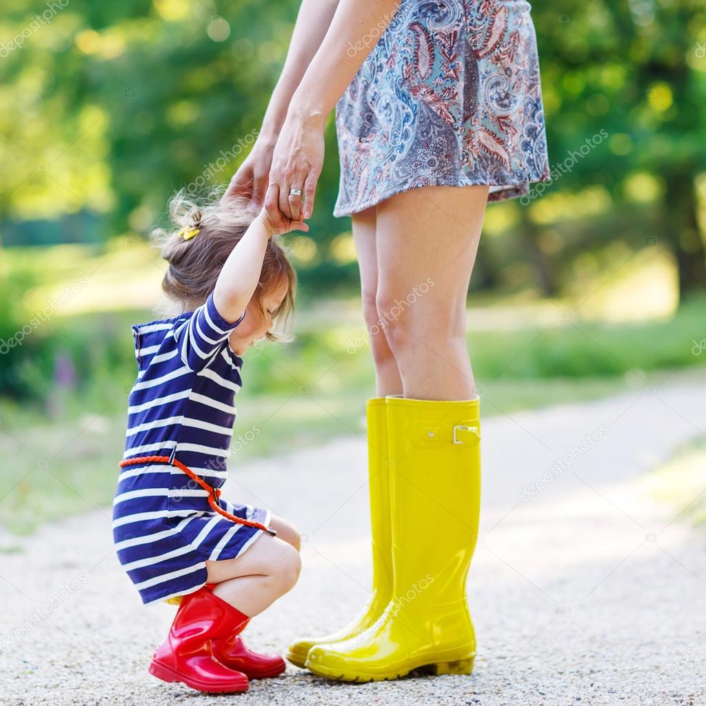 mother and little adorable child girl in rubber boots having fun