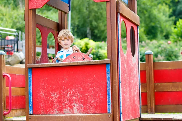 Criança menino finge dirigir um carro imaginário no parque infantil — Fotografia de Stock