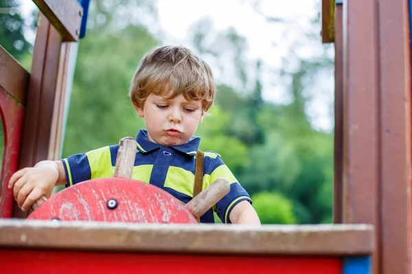 Niño niño finge conducir un coche imaginario en el parque infantil — Foto de Stock