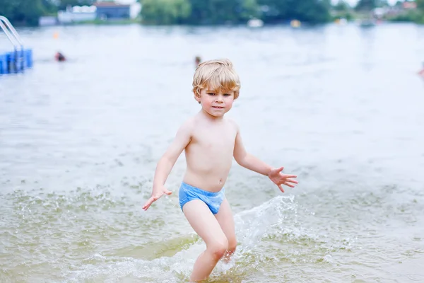 Pequeño chico rubio divirtiéndose con salpicaduras en un lago, outdoo — Foto de Stock