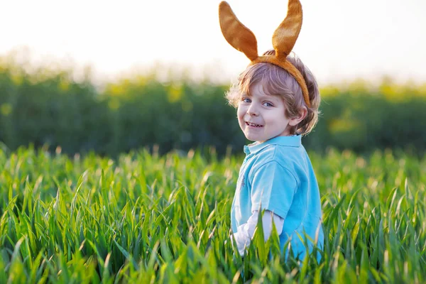 Ragazzino carino con orecchie di coniglio pasquali in erba verde — Foto Stock