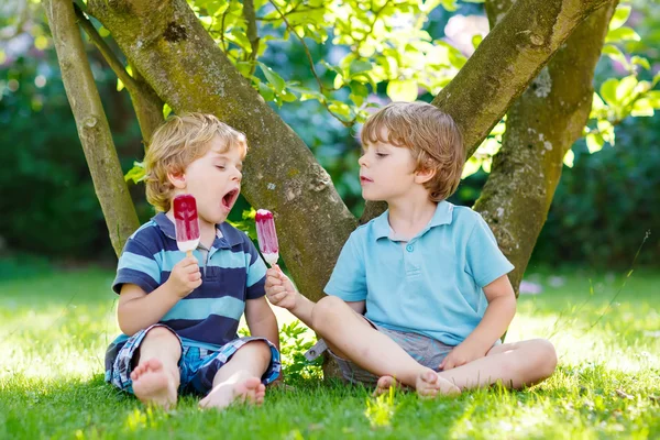 Zwei kleine Geschwister essen rotes Eis im heimischen Garten. — Stockfoto