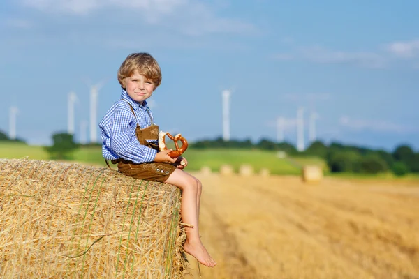 Funny little kid boy sitting on hay stack  and eating pretzel — Stock Photo, Image