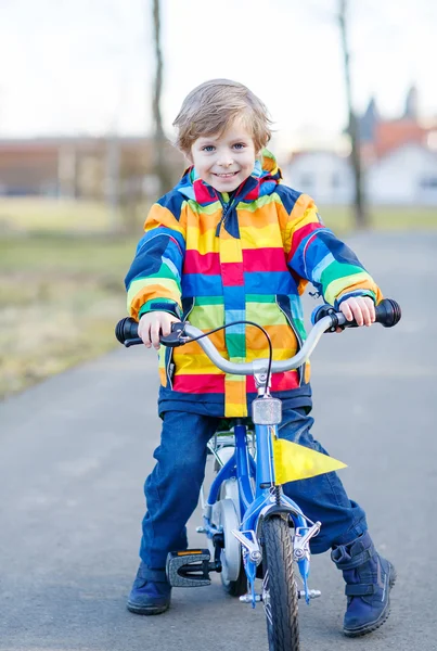 Kid boy in safety helmet and colorful raincoat riding bike, outd — Stock Photo, Image