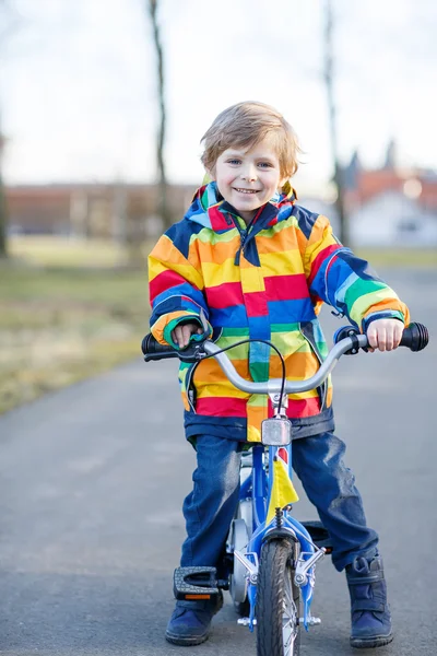 Kid jongen in veiligheidshelm en kleurrijke regenjas rijden fiets, outd — Stockfoto