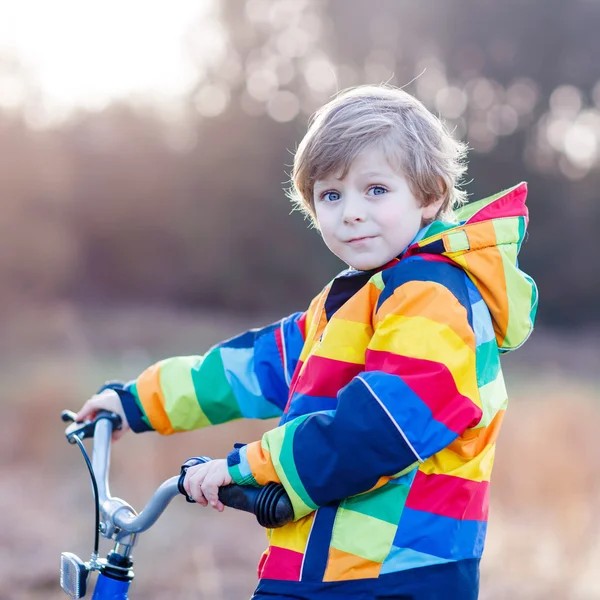 Anak laki-laki dengan helm keselamatan dan jas hujan berwarna-warni naik sepeda, outd — Stok Foto