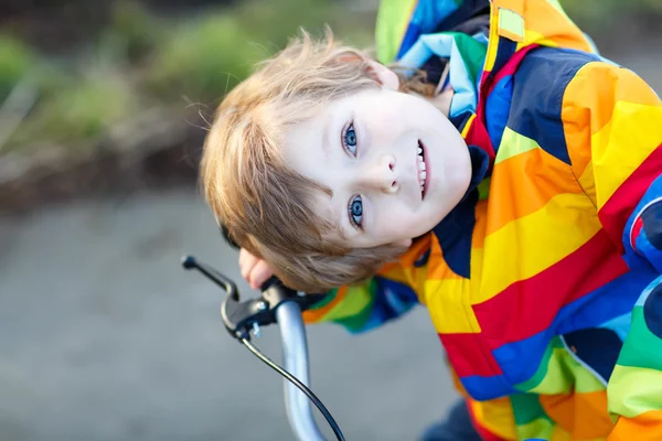 Unge pojken i skyddshjälm och färgglada regnrock ridning cykel, utomhus — Stockfoto