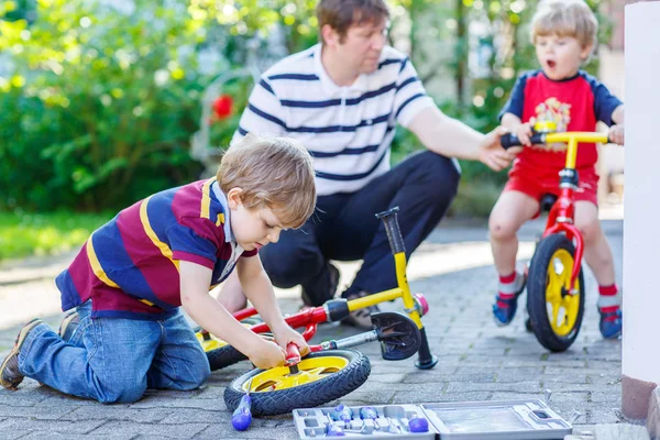 Pai ensinando dois garotos a consertar a corrente em bicicletas — Fotografia de Stock