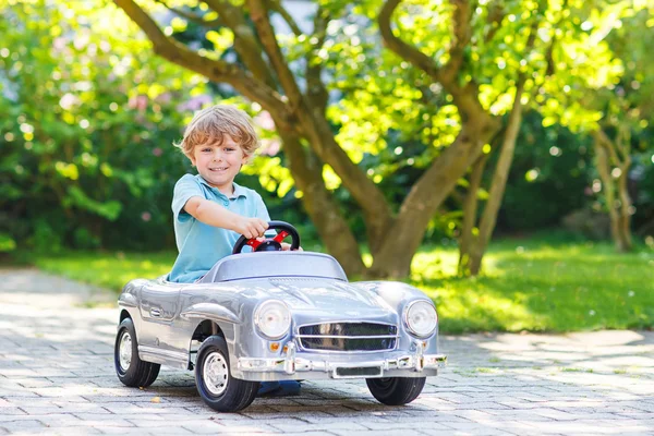 Menino dirigindo brinquedo grande carro velho, ao ar livre — Fotografia de Stock