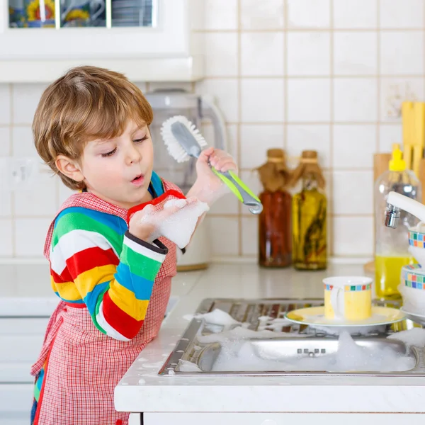 Criança adorável lavar pratos na cozinha doméstica . — Fotografia de Stock