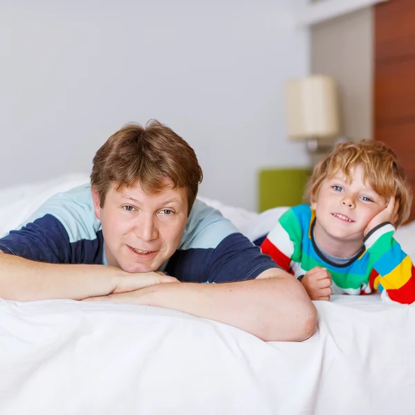 Pai e seu filho pequeno relaxando e descansando na cama branca — Fotografia de Stock