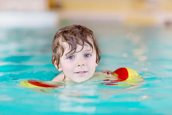 Mały chłopiec dziecko z swimmies uczyć się pływać w krytym basenem — Zdjęcie stockowe