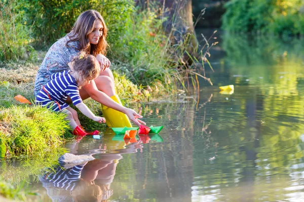 Adorable niña y su madre jugando con barcos de papel en una r — Stock fotografie