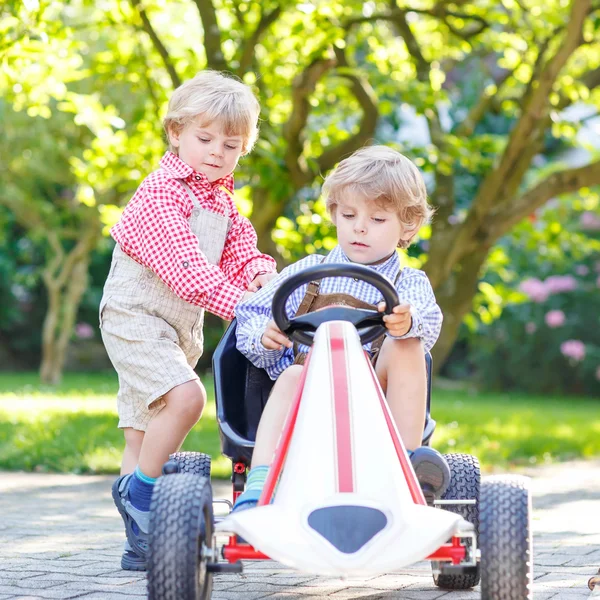 Two little sibling boys playing with pedal car in home's garden — Stock Photo, Image