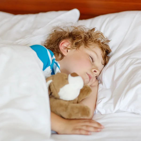 Μικρό ξανθό παιδί που κοιμάται στο κρεβάτι του με το παιχνίδι. — Φωτογραφία Αρχείου