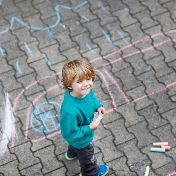 Kleine blonde jongen schilderen met kleurrijke krijtjes buitenshuis — Stockfoto