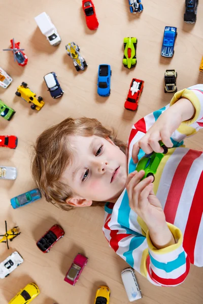 Grappige kleine jongen speelt met veel speelgoed auto's binnen — Stockfoto