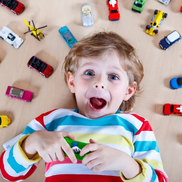 Очаровательный маленький мальчик играет с кучей игрушечных машин в помещении — стоковое фото