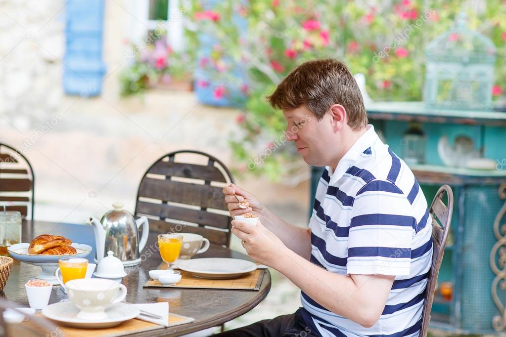 young man having breakfast outside in summer 