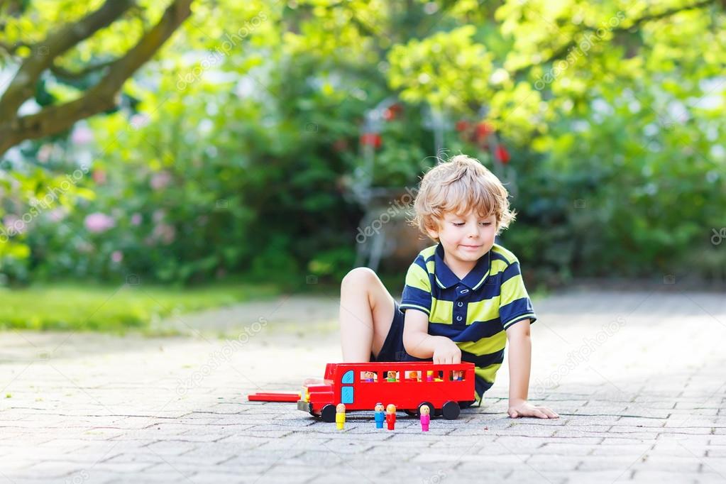 Little blond kid boy in colorful clothes playing with red wooden