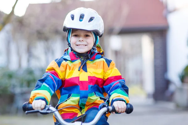 Kid boy in safety helmet and colorful raincoat riding bike, outd — Stock Photo, Image