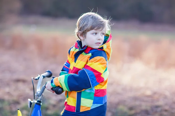 Unge pojken i skyddshjälm och färgglada regnrock ridning cykel, utomhus — Stockfoto