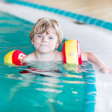 little kid boy with swimmies learning to swim in an indoor pool clipart