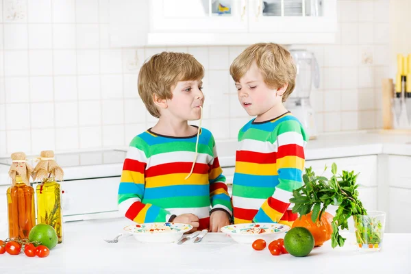 Dos niños comiendo espaguetis en la cocina doméstica . — Foto de Stock