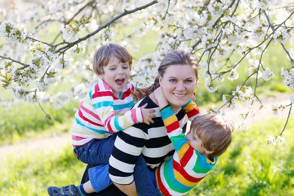 Junge Mutter und zwei kleine Zwillinge Jungen haben Spaß in blühenden ga — Stockfoto